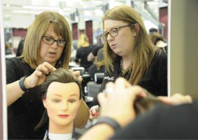 A hairdressing tutor and student practising on a wig. 