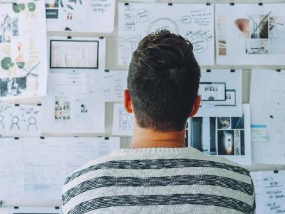 A man looks at a whiteboard covered in documents. 