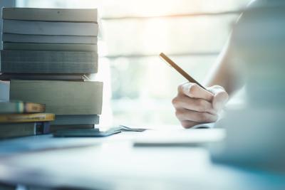 Person hand holding a pen over paper at a desk surrounded with books